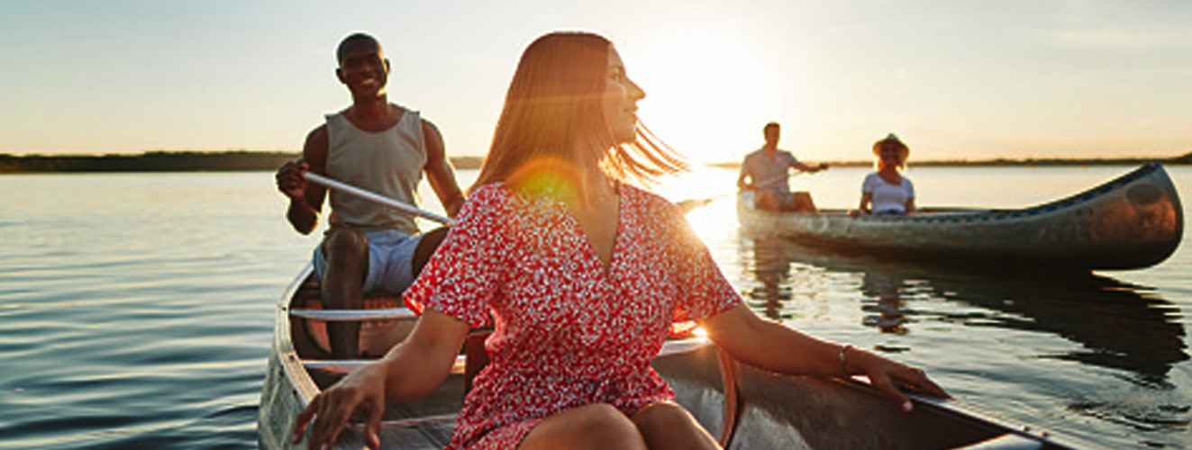 Smiling young woman looking at the scenic view while canoeing with her boyfriend and another couple on a lake on a sunny summer afternoon