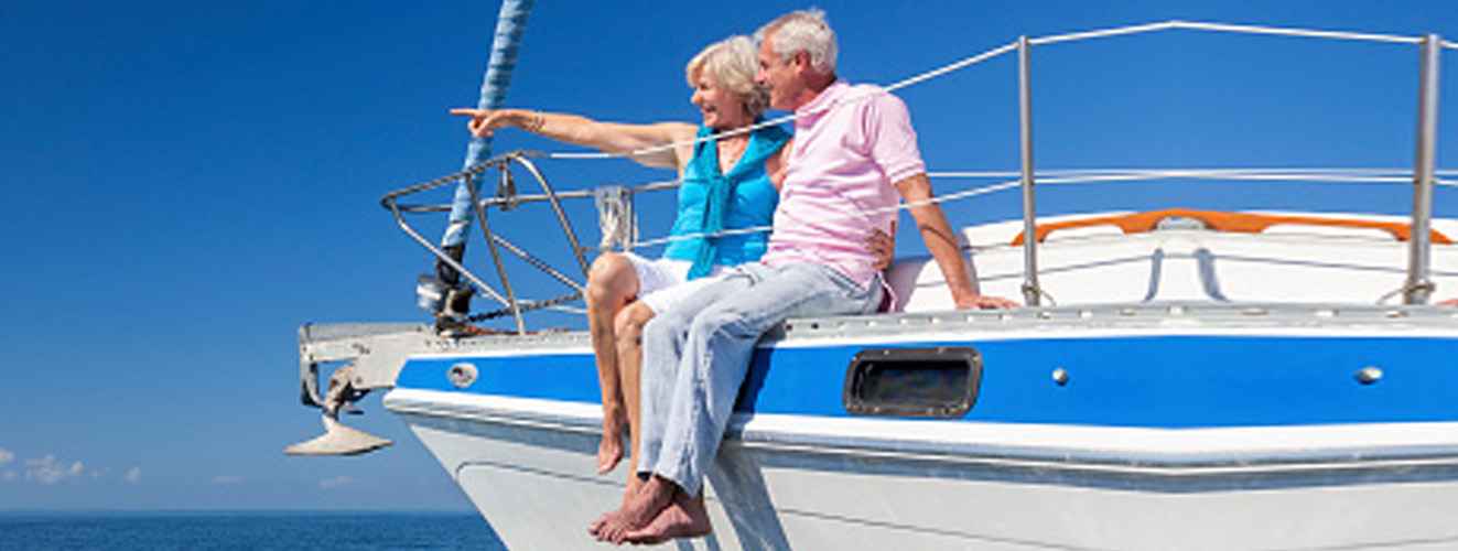 A happy senior couple sitting on the side of a sail boat on a calm blue sea looking and pointing to a clear horizon